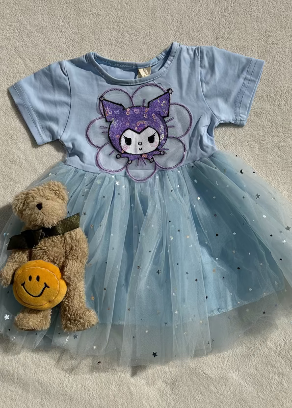 Children's dress with a cartoon character and a teddy bear with a smiley face toy on a beige surface