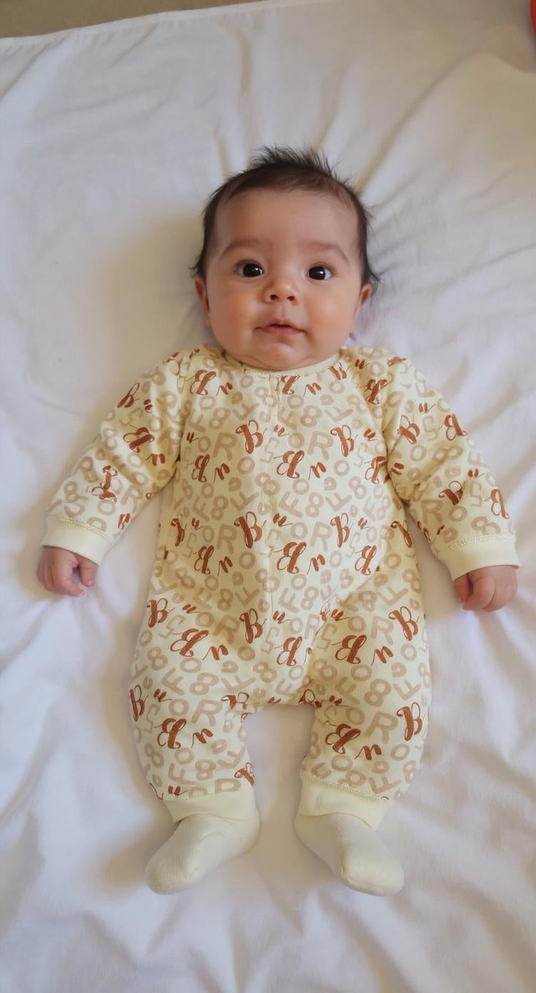 Baby wearing a patterned onesie lying on a white surface