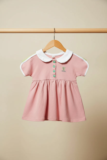 Pink dress with white collar and green buttons on a black background