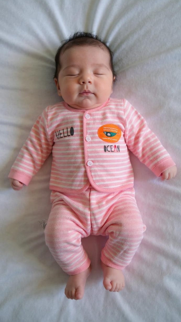 Newborn baby in a pink striped outfit lying on a white surface