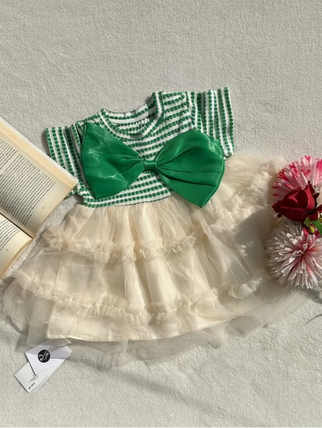 Children's dress with green bow and white skirt on a textured surface with flowers and an open book.