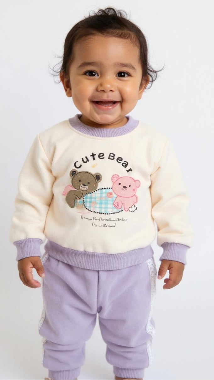 Child wearing a cream sweater with teddy bear design and lavender pants on a white background